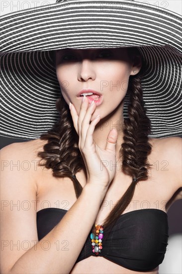 Beautiful cheerful girl in a summer beach striped hat. The beauty of the face. Photos shot in the studio