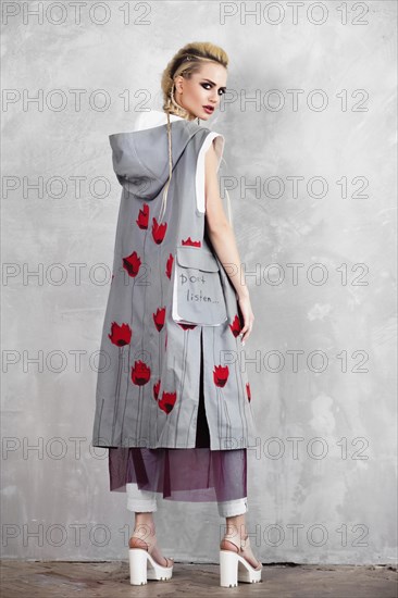 Creative unusual blond girl in designer clothes and braids on her head posing in the studio