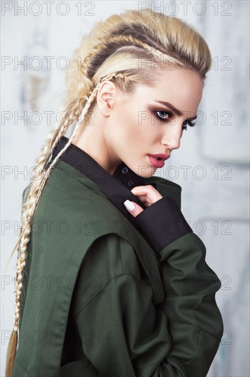 Creative unusual blond girl in designer clothes and braids on her head posing in the studio