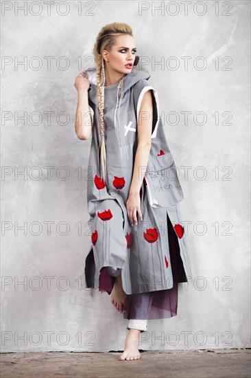 Creative unusual blond girl in designer clothes and braids on her head posing in the studio