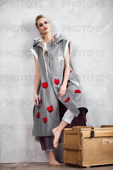 Creative unusual blond girl in designer clothes and braids on her head posing in the studio