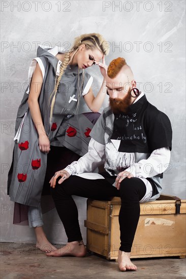 Creative unusual blond girl and red-haired man in designer clothes and braids on their heads posing in the studio