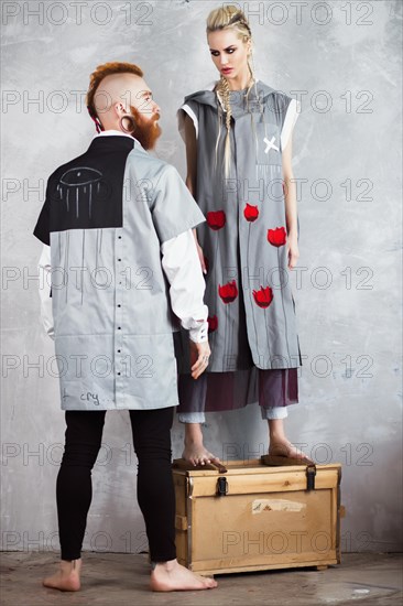 Creative unusual blond girl and red-haired man in designer clothes and braids on their heads posing in the studio