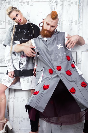 Creative unusual blond girl and red-haired man in designer clothes and braids on their heads posing in the studio