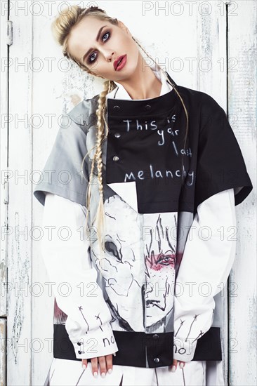 Creative unusual blond girl in designer clothes and braids on her head posing in the studio