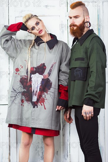 Creative unusual blond girl and red-haired man in designer clothes and braids on their heads posing in the studio