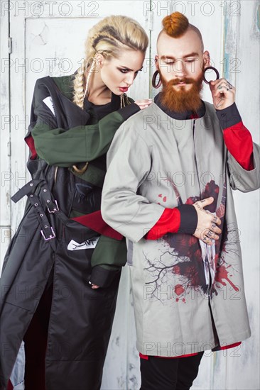 Creative unusual blond girl and red-haired man in designer clothes and braids on their heads posing in the studio