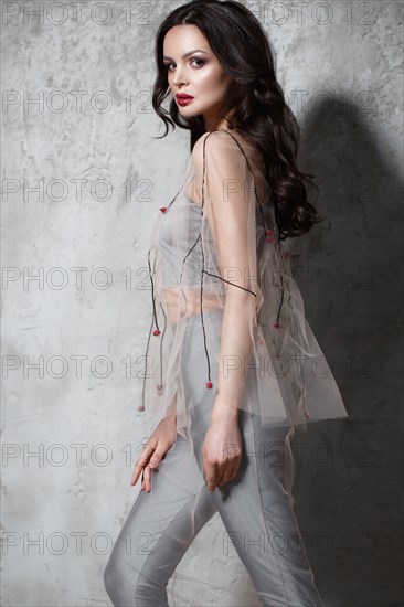 Beautiful girl in designer fashionable transparent clothes posing in studio. Beauty of face and body