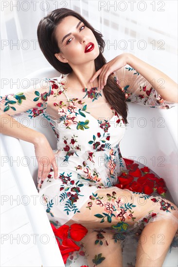 Beautiful girl in a summer dress in the bathroom with flowers. Beauty face. Photo taken in the studio