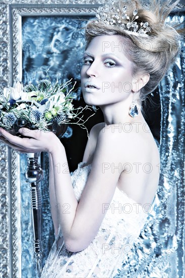 Beautiful girl in white dress in the image of the Snow Queen with a crown on her head. Picture taken in the studio with decorations