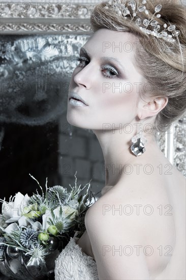 Beautiful girl in white dress in the image of the Snow Queen with a crown on her head. Picture taken in the studio with decorations