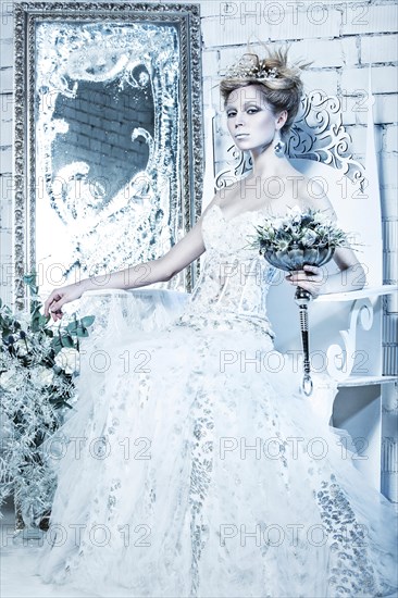 Beautiful girl in white dress in the image of the Snow Queen with a crown on her head. Picture taken in the studio with decorations