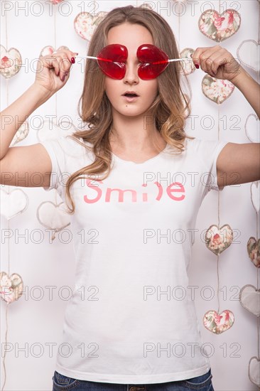 Valentines Day. Funny beautiful Woman holding candy in the form of heart. Beauty face. Picture taken in the studio with decorations