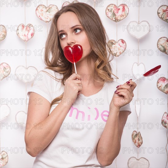 Valentines Day. Funny beautiful Woman holding candy in the form of heart. Beauty face. Picture taken in the studio with decorations