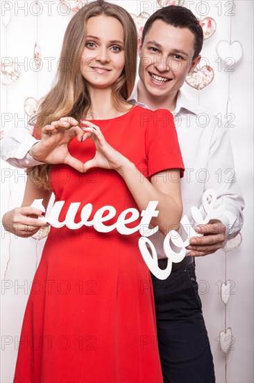 Beautiful young couple in love with the words Sweet love showing the form of heart hands. Valentine's Day. Picture taken in the studio