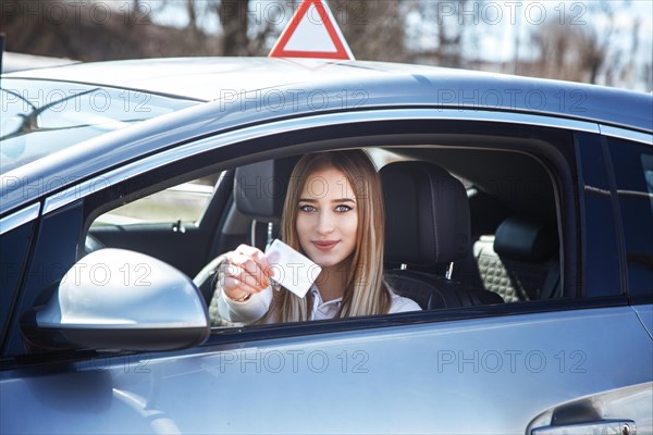 Joyful girl driving a training car with a drivers license card in her hands