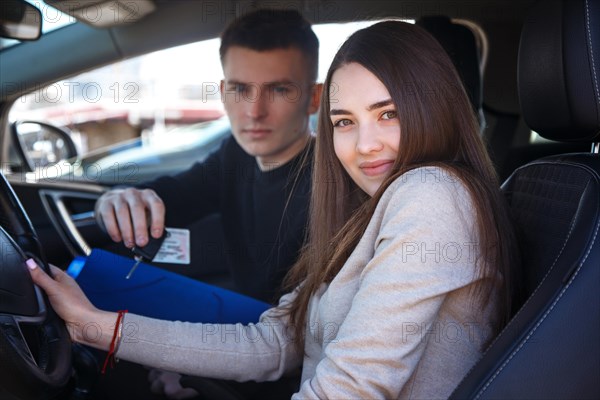 Happy girl in a new car receives a drivers license and keys from a young man