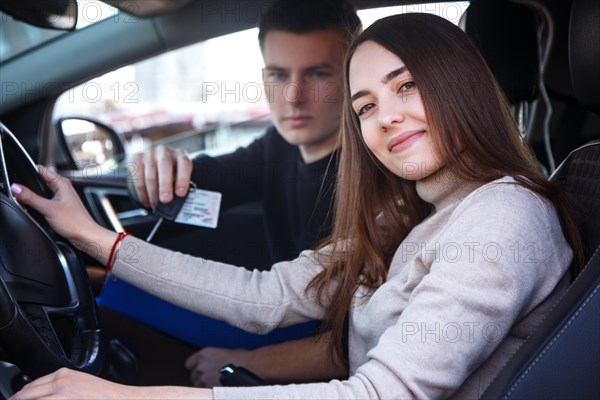 Happy girl in a new car receives a drivers license and keys from a young man