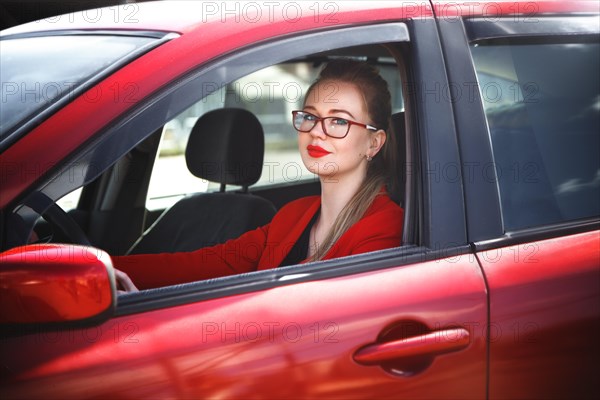 Young beautiful happy woman in red sitting at the wheel new training car