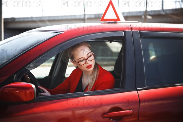 Young beautiful happy woman in red sitting at the wheel new training car