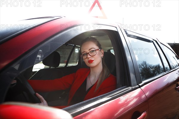 Young beautiful happy woman in red sitting at the wheel new training car