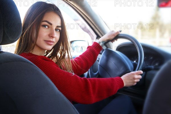 Young beautiful happy woman in red sitting at the wheel new training car