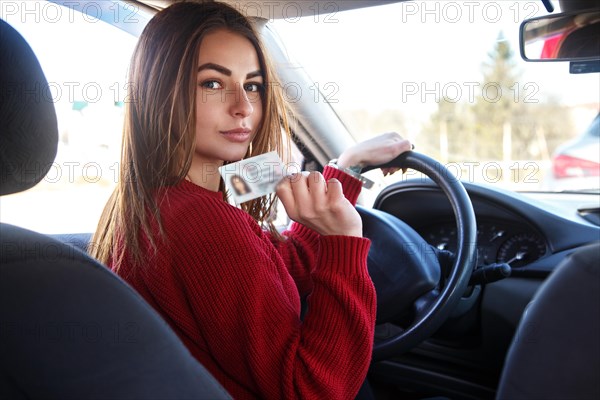 Joyful girl driving a training car with a drivers license card in her hands