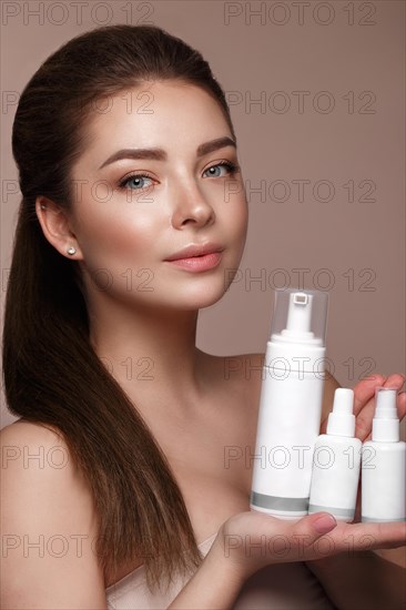 Beautiful young girl with natural nude make-up with cosmetic in hands. Beauty face. Photo taken in studio