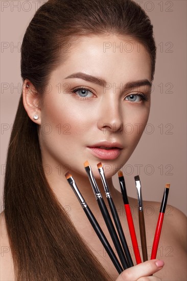 Beautiful young girl with natural nude make-up with cosmetic tools in hands. Beauty face. Photo taken in studio