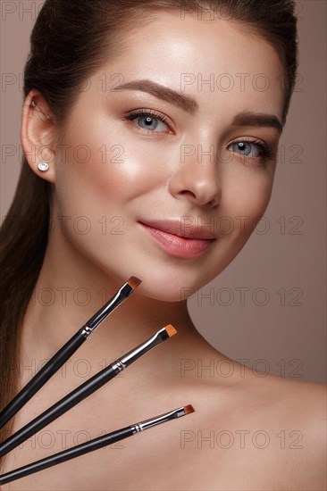 Beautiful young girl with natural nude make-up with cosmetic tools in hands. Beauty face. Photo taken in studio