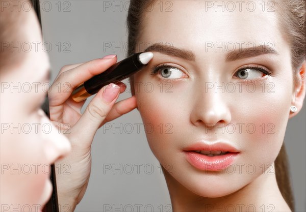 Beautiful girl makes herself a make-up in the mirror. Beauty face. Photo taken in studio