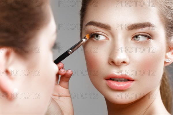 Beautiful girl makes herself a make-up in the mirror. Beauty face. Photo taken in studio