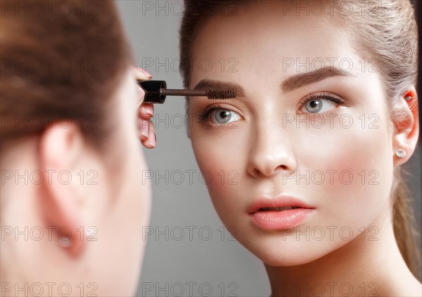 Beautiful girl makes herself a make-up in the mirror. Beauty face. Photo taken in studio