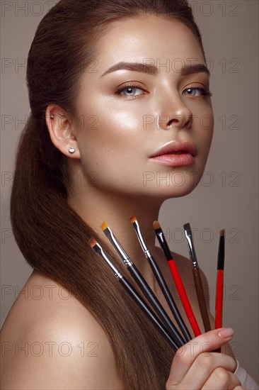 Beautiful young girl with natural nude make-up with cosmetic tools in hands. Beauty face. Photo taken in studio