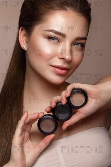 Beautiful young girl with natural nude make-up with cosmetic in hands. Beauty face. Photo taken in studio