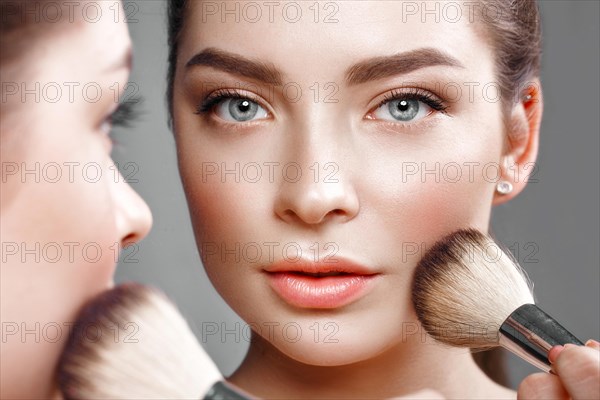 Beautiful girl makes herself a make-up in the mirror. Beauty face. Photo taken in studio