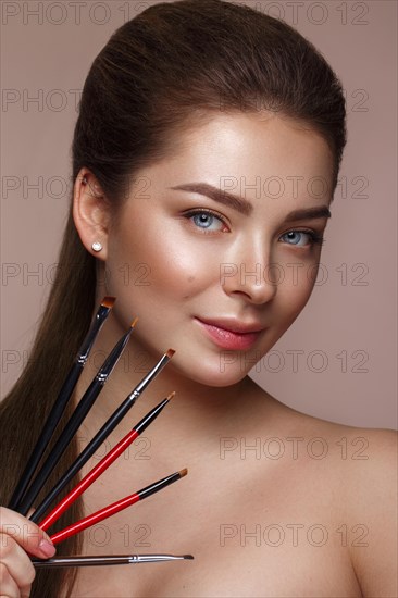 Beautiful young girl with natural nude make-up with cosmetic tools in hands. Beauty face. Photo taken in studio