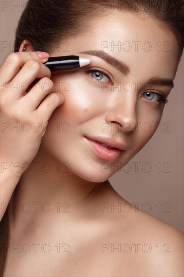 Beautiful young girl with natural nude make-up and highlighter pencil. Beauty face. Photo taken in studio