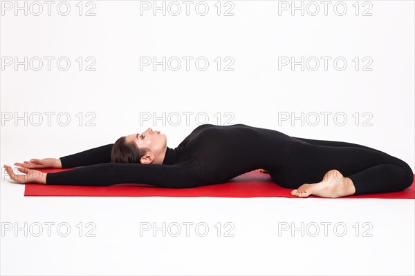 Beautiful athletic girl in black suit doing yoga. Supta Virasana asana lightning sleeping pose. Isolated on white background