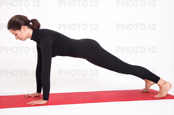 Beautiful athletic girl in black suit doing yoga. Kumbhasana asana plank pose. Isolated on white background