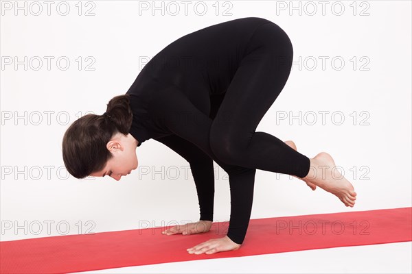 Beautiful athletic girl in a black suit doing yoga. Kakasana asana