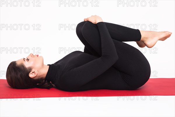 Beautiful athletic girl in black suit doing yoga. apanasana asana apan pose. Isolated on white background