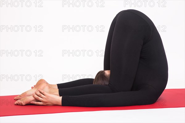 Beautiful athletic girl in a black suit doing yoga. karnapidasana asana