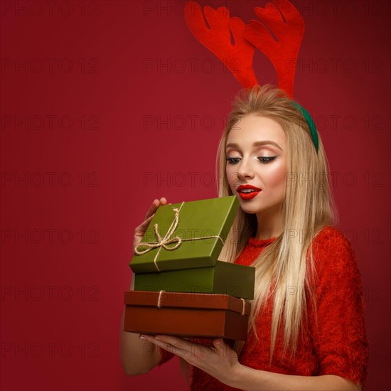 Beautiful blonde girl in a New Year's image with boxes of gifts in hands and deer horns on her head. Beauty face with festive makeup. Photo taken in the studio