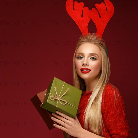 Beautiful blonde girl in a New Year's image with boxes of gifts in hands and deer horns on her head. Beauty face with festive makeup. Photo taken in the studio
