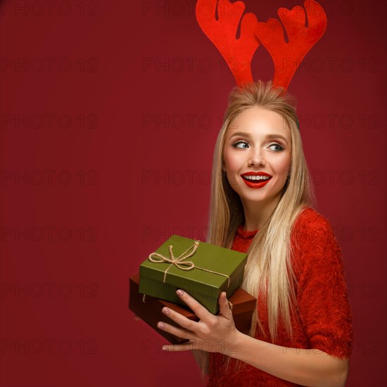 Beautiful blonde girl in a New Year's image with boxes of gifts in hands and deer horns on her head. Beauty face with festive makeup. Photo taken in the studio