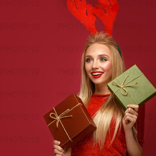 Beautiful blonde girl in a New Year's image with boxes of gifts in hands and deer horns on her head. Beauty face with festive makeup. Photo taken in the studio