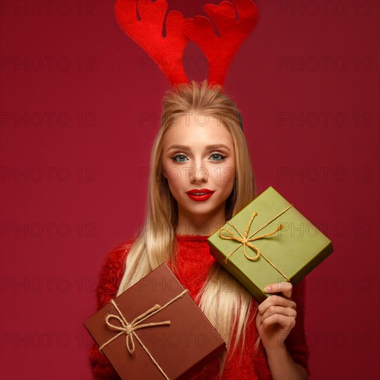 Beautiful blonde girl in a New Year's image with boxes of gifts in hands and deer horns on her head. Beauty face with festive makeup. Photo taken in the studio