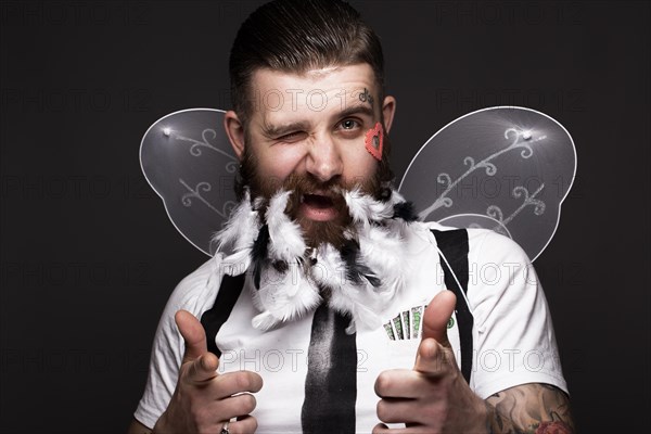 Funny bearded man with feathers and wings in the image of Cupid Valentine's Day. Portrait shot in studio