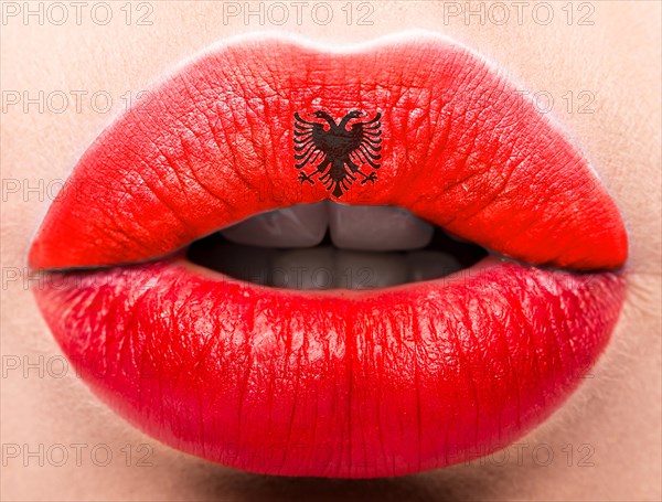 Female lips close up with a picture of the flag of Albania. Red and black emblem
